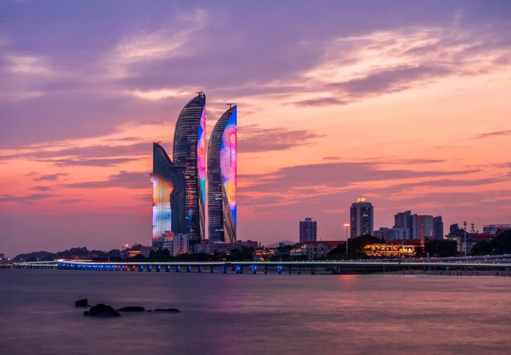 Xiamen Twin Towers at Sunset – Xiamen Shimao Twin Towers illuminated at dusk, reflecting colorful lights over the sea with a dramatic sunset sky and modern city skyline
