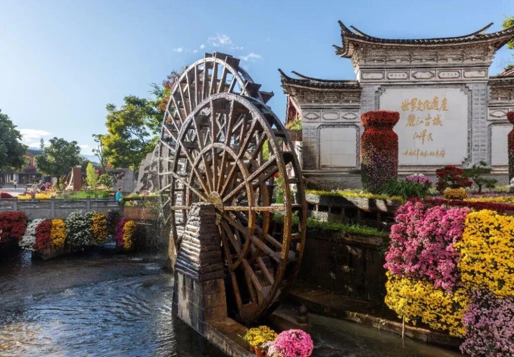 Lijiang Old Town Waterwheel – traditional wooden waterwheel and historic architecture surrounded by colorful flowers