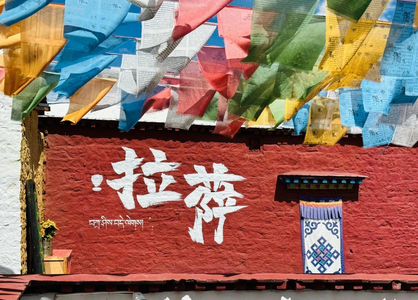 Muro de un patio con banderas de oración tibetanas de colores ondeando sobre una pared roja tradicional con escritura tibetana en Lhasa - Guía de viaje al Tíbet: mejores rutas, consejos e itinerarios 2026 - The China Journey Muro de un patio con banderas de oración tibetanas de colores ondeando sobre una pared roja tradicional con escritura tibetana en Lhasa - Guía de viaje al Tíbet: mejores rutas, consejos e itinerarios 2026 - The China Journey