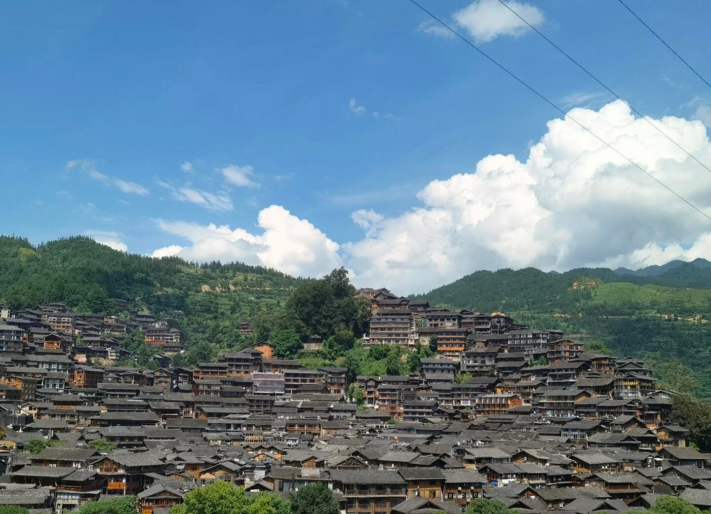 Xijiang Miao Köyü gündüz panoraması; dağlar ve açık gökyüzü önünde yamacı kaplayan yoğun ahşap evler - Guizhou Gezi Rehberi: Rotalar, İpuçları ve Gezi Planları 2026 - The China Journey Xijiang Miao Köyü gündüz panoraması; dağlar ve açık gökyüzü önünde yamacı kaplayan yoğun ahşap evler - Guizhou Gezi Rehberi: Rotalar, İpuçları ve Gezi Planları 2026 - The China Journey