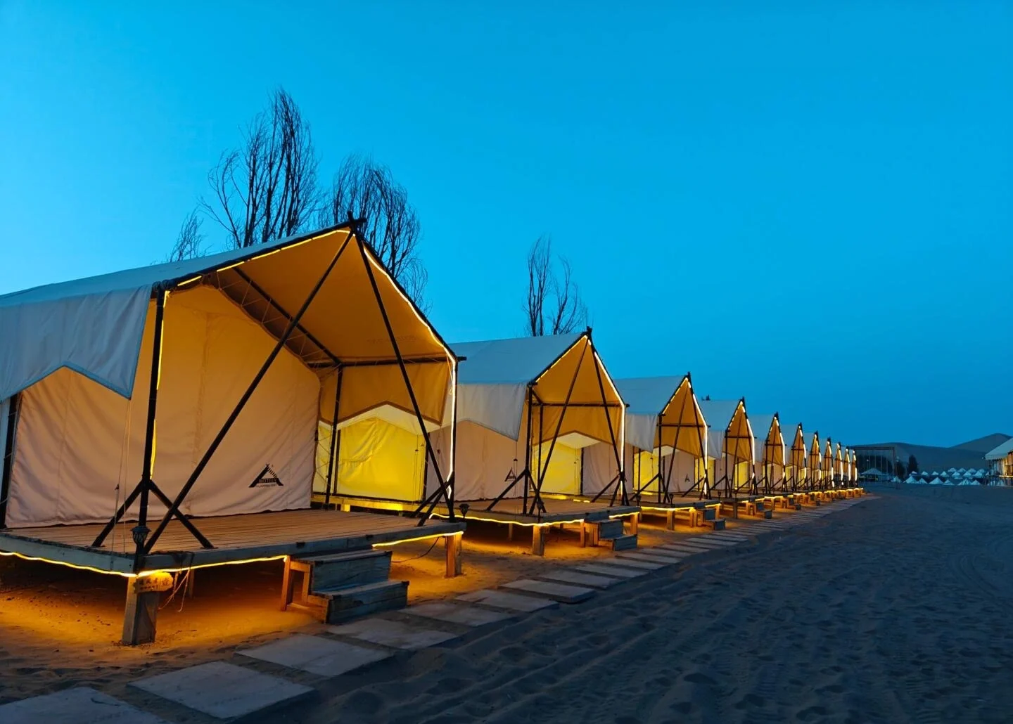 Dunhuang-ørkenens glampingtelte i skumringen. Række af oplyste luksustelte i sandørkenen under blå aftenhimmel - Overnatning i Dunhuang: Bedste områder og hoteller 2026 - The China Journey Dunhuang-ørkenens glampingtelte i skumringen. Række af oplyste luksustelte i sandørkenen under blå aftenhimmel - Overnatning i Dunhuang: Bedste områder og hoteller 2026 - The China Journey